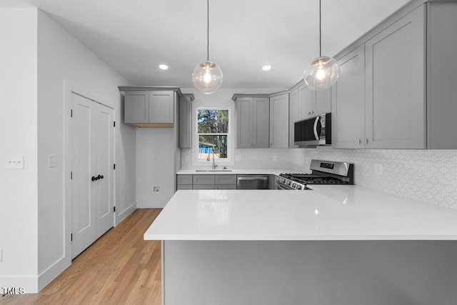 kitchen with kitchen peninsula, appliances with stainless steel finishes, decorative light fixtures, and light hardwood / wood-style flooring