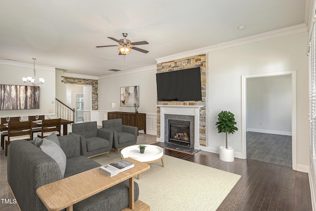 living room featuring ceiling fan with notable chandelier, a stone fireplace, dark hardwood / wood-style flooring, and crown molding