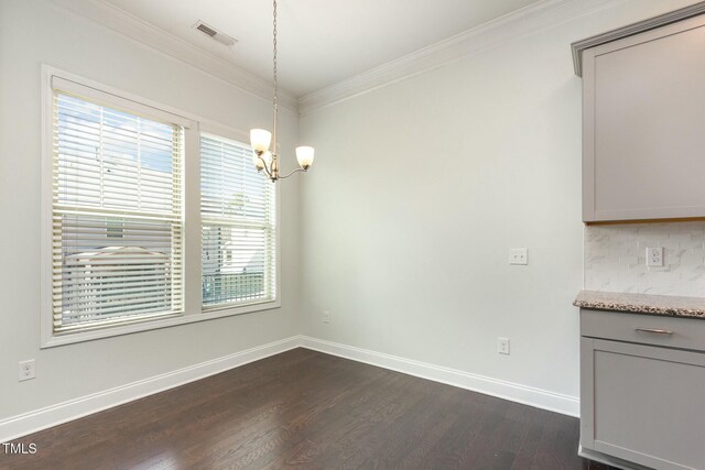 unfurnished dining area with visible vents, dark wood finished floors, crown molding, baseboards, and a chandelier