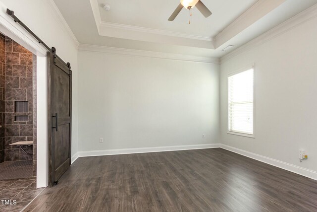 spare room featuring a barn door, a ceiling fan, dark wood-type flooring, and a raised ceiling