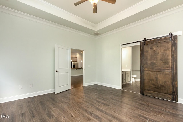 unfurnished bedroom featuring a barn door, baseboards, dark wood-style flooring, and a tray ceiling