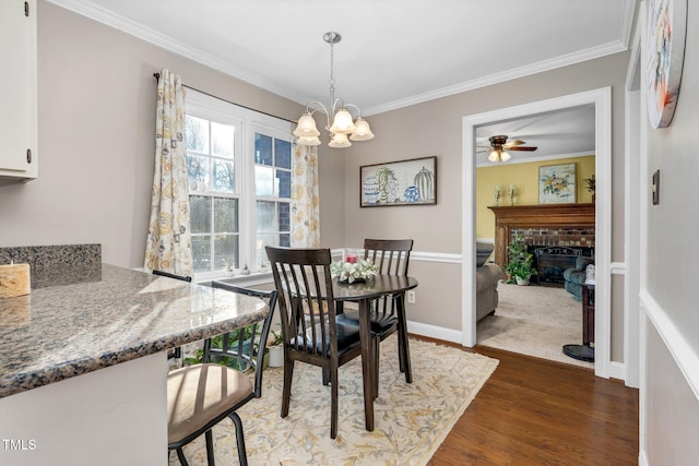 dining room featuring ceiling fan with notable chandelier, dark hardwood / wood-style flooring, crown molding, and a brick fireplace