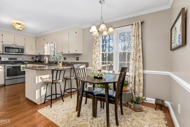 kitchen with dark stone counters, hardwood / wood-style flooring, appliances with stainless steel finishes, a notable chandelier, and kitchen peninsula