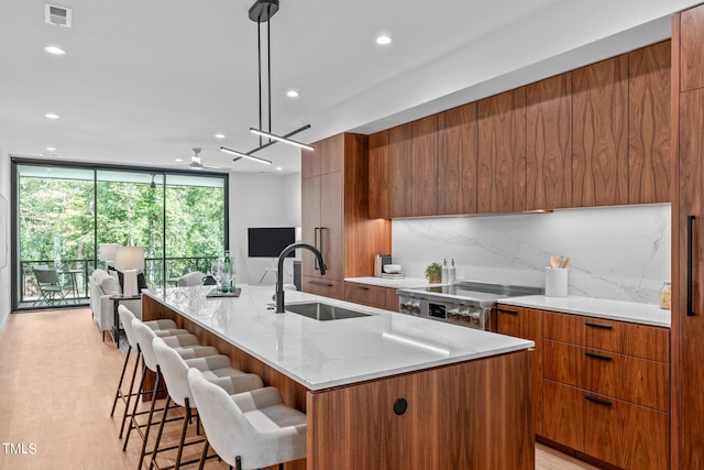 kitchen with stove, light wood-type flooring, sink, decorative light fixtures, and an island with sink