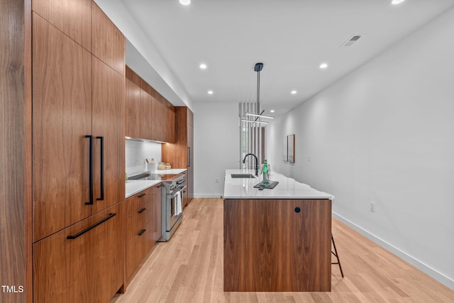 kitchen with sink, a spacious island, decorative light fixtures, high end stainless steel range, and light wood-type flooring