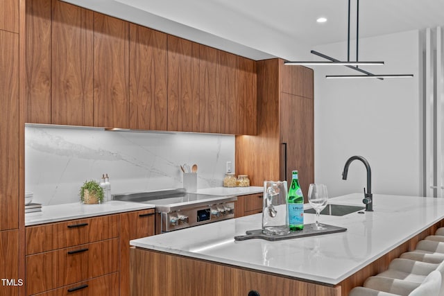 kitchen with sink, a notable chandelier, decorative light fixtures, a kitchen island with sink, and stainless steel stove