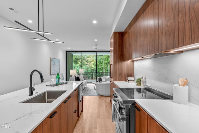 kitchen with high end stove, light stone countertops, light hardwood / wood-style flooring, and sink