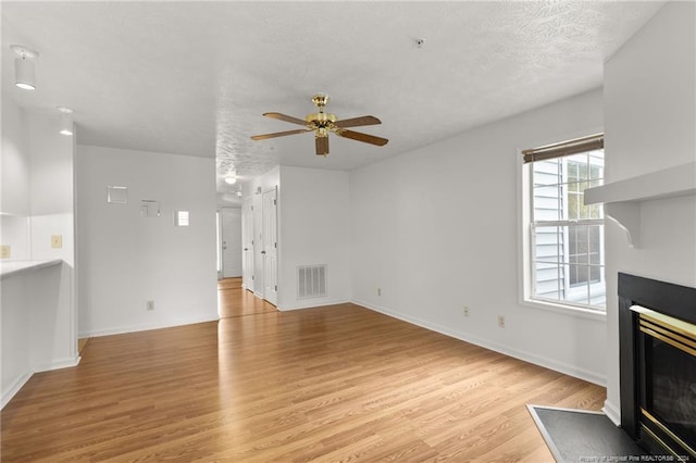 unfurnished living room with ceiling fan, a textured ceiling, and light wood-type flooring