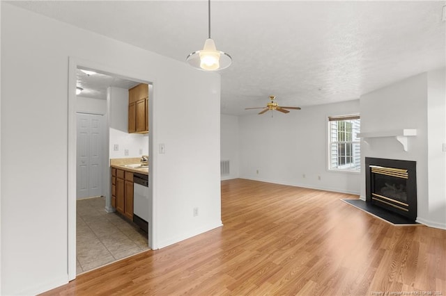 unfurnished living room featuring a textured ceiling, ceiling fan, sink, and light hardwood / wood-style flooring