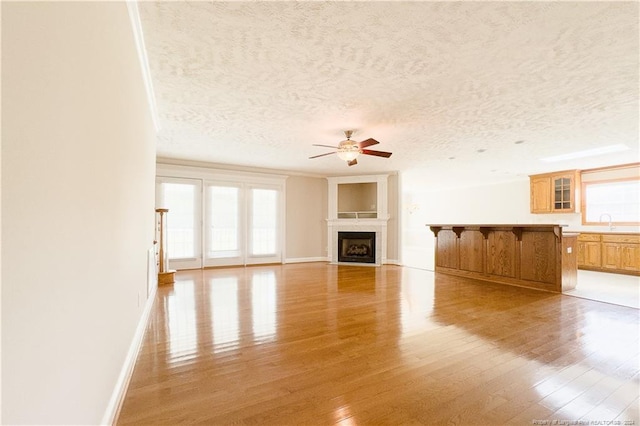 unfurnished living room with ceiling fan, light hardwood / wood-style flooring, a textured ceiling, and sink