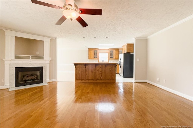 unfurnished living room featuring ceiling fan, ornamental molding, a textured ceiling, and light hardwood / wood-style flooring