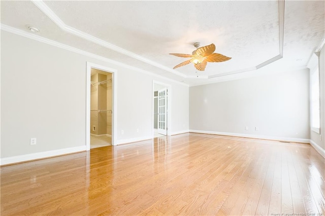 spare room featuring ornamental molding, a textured ceiling, a tray ceiling, ceiling fan, and light hardwood / wood-style flooring