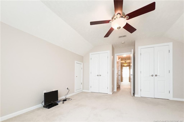 unfurnished bedroom featuring light colored carpet, multiple closets, and vaulted ceiling