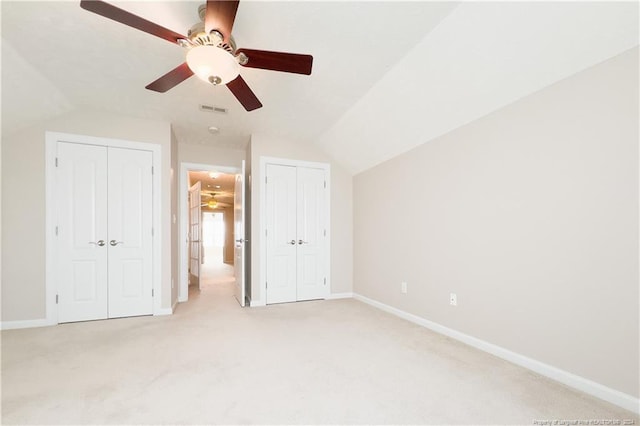 unfurnished bedroom featuring ceiling fan, lofted ceiling, light carpet, and two closets