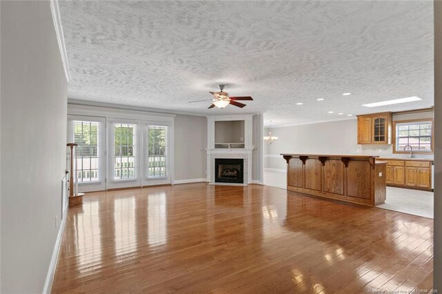 4419 Cameron Rd, Hope Mills, NC 28348 - unfurnished living room featuring light wood-style flooring, a ceiling fan, a fireplace with flush hearth, crown molding, and a textured ceiling