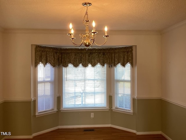 unfurnished dining area with a notable chandelier, a healthy amount of sunlight, wood-type flooring, and crown molding