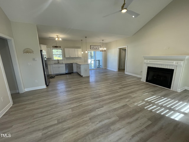 unfurnished living room with a tiled fireplace, light hardwood / wood-style flooring, ceiling fan with notable chandelier, and sink