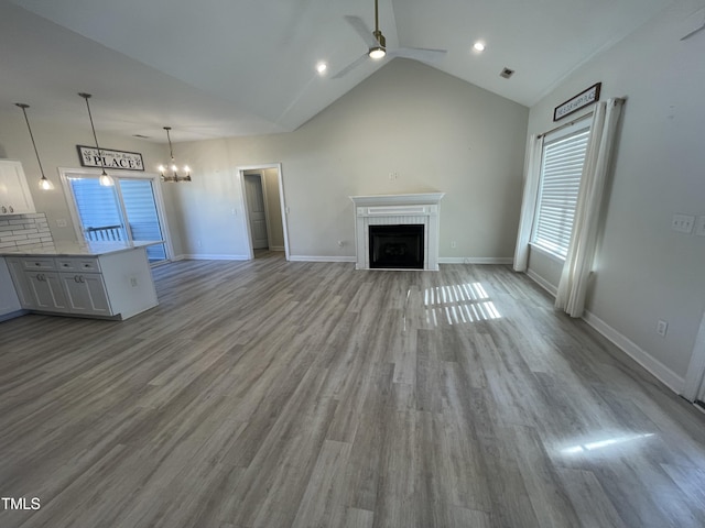 unfurnished living room featuring light hardwood / wood-style flooring, high vaulted ceiling, and ceiling fan with notable chandelier