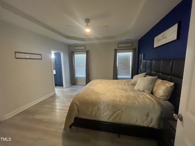 bedroom with ceiling fan, a raised ceiling, and wood-type flooring