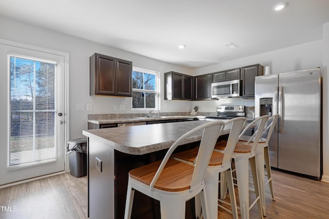 80 Bella Vita Way, Angier, NC 27501 - kitchen with stainless steel appliances, dark brown cabinetry, a kitchen bar, light wood-style floors, and a center island