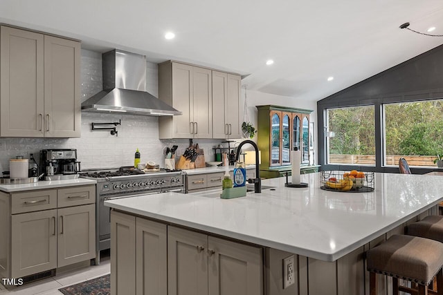 kitchen featuring double oven range, lofted ceiling, a center island with sink, and wall chimney exhaust hood