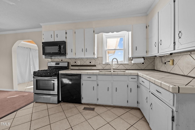 kitchen featuring black appliances, white cabinets, sink, light tile patterned floors, and tile counters