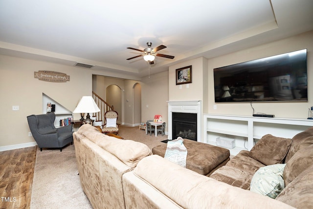 living room with a raised ceiling, ceiling fan, and light hardwood / wood-style flooring