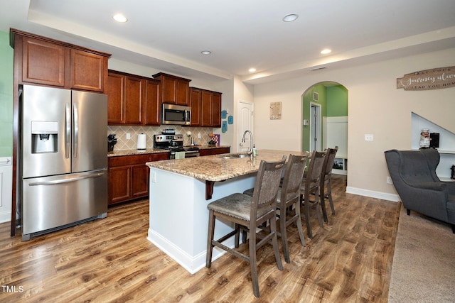 kitchen featuring a breakfast bar, hardwood / wood-style floors, an island with sink, and stainless steel appliances