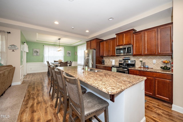 kitchen with dark wood-type flooring, stainless steel appliances, a center island with sink, and sink