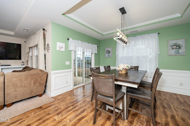 dining space with a raised ceiling, crown molding, and wood-type flooring