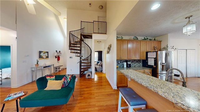 kitchen featuring pendant lighting, a high ceiling, light hardwood / wood-style flooring, stainless steel fridge, and light stone countertops