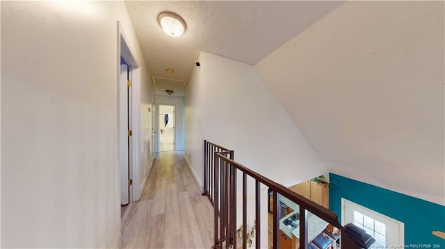 hallway featuring a textured ceiling, light wood-type flooring, and vaulted ceiling