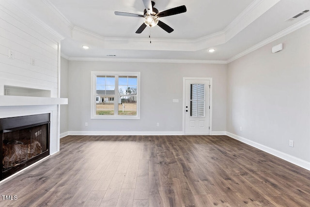 unfurnished living room featuring a large fireplace, dark hardwood / wood-style floors, a tray ceiling, and crown molding