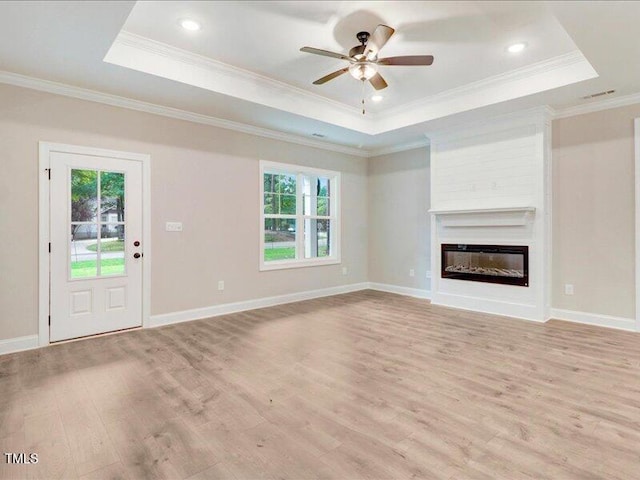 unfurnished living room featuring a fireplace, a healthy amount of sunlight, light hardwood / wood-style flooring, and a tray ceiling