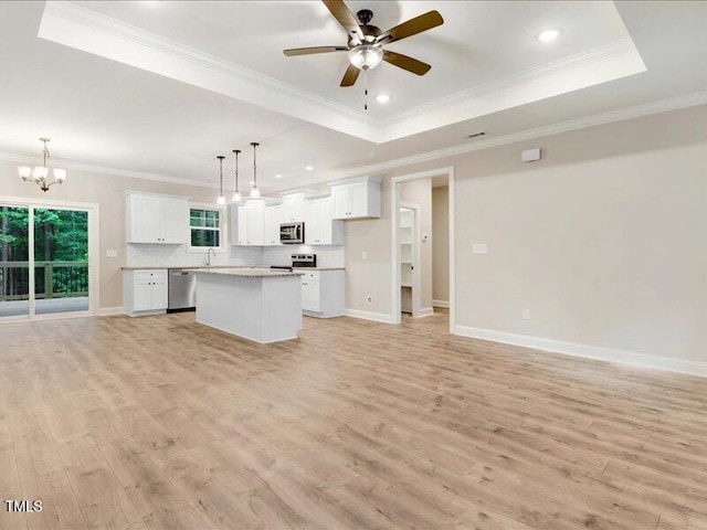 kitchen with white cabinets, a tray ceiling, decorative light fixtures, a kitchen island, and stainless steel appliances