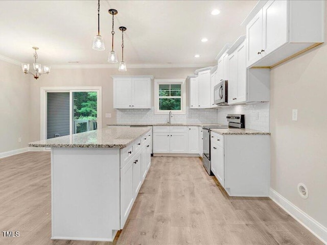 kitchen featuring ornamental molding, appliances with stainless steel finishes, decorative light fixtures, a kitchen island, and white cabinetry