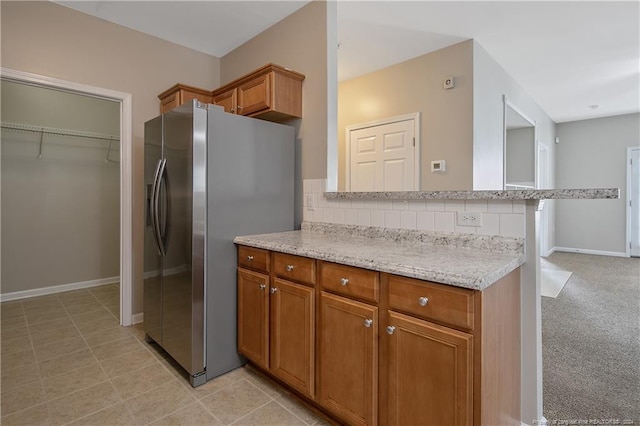 kitchen featuring decorative backsplash, stainless steel fridge, light colored carpet, and light stone counters