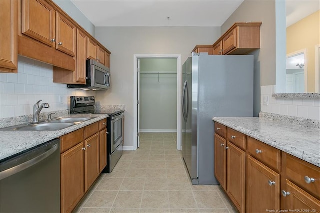 kitchen with light stone countertops, stainless steel appliances, tasteful backsplash, and sink