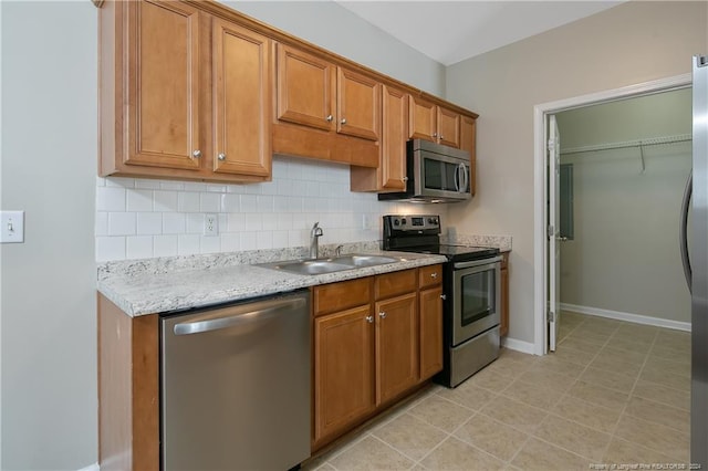 kitchen with appliances with stainless steel finishes, backsplash, light stone counters, sink, and light tile patterned floors