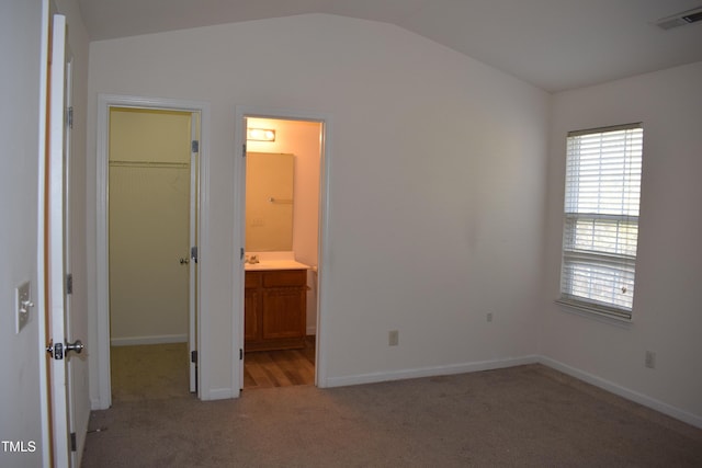 unfurnished bedroom featuring lofted ceiling, a walk in closet, connected bathroom, light colored carpet, and a closet