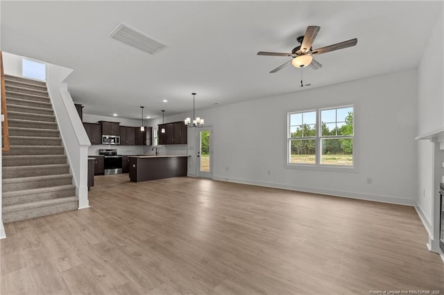 unfurnished living room featuring recessed lighting, stairs, ceiling fan with notable chandelier, a glass covered fireplace, and visible vents