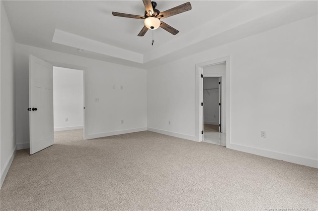 unfurnished bedroom featuring a tray ceiling, baseboards, light carpet, a spacious closet, and a ceiling fan