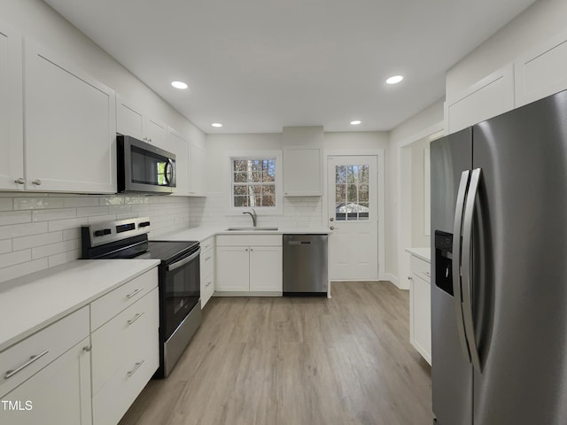 kitchen featuring sink, light hardwood / wood-style flooring, decorative backsplash, white cabinets, and appliances with stainless steel finishes