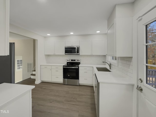 kitchen with hardwood / wood-style floors, backsplash, white cabinets, sink, and appliances with stainless steel finishes