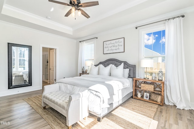 bedroom with ornamental molding, ceiling fan, wood finished floors, and a raised ceiling