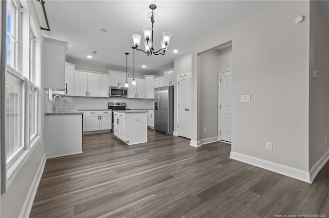 kitchen featuring white cabinetry, hanging light fixtures, appliances with stainless steel finishes, a kitchen island, and decorative backsplash