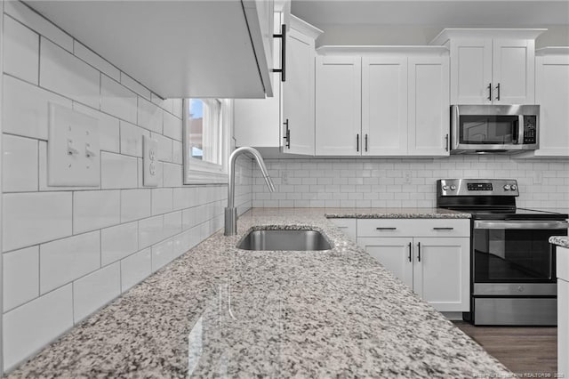 kitchen featuring sink, appliances with stainless steel finishes, white cabinetry, tasteful backsplash, and light stone countertops