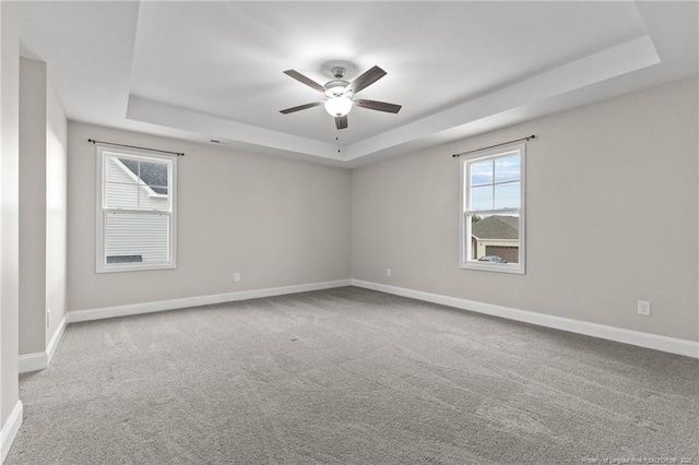 spare room with a raised ceiling, light carpet, and ceiling fan