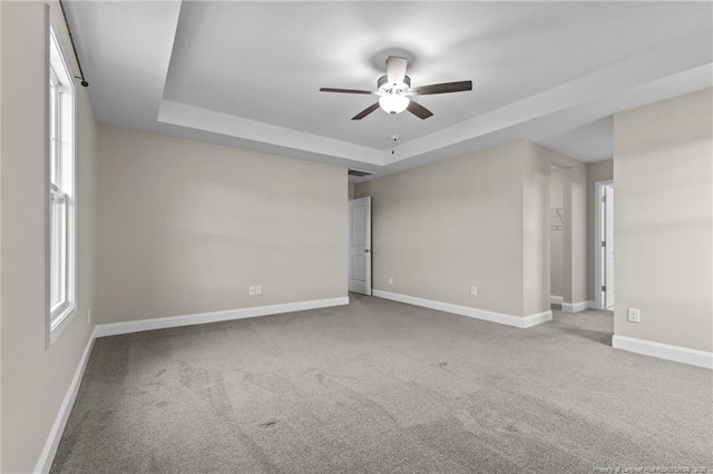 empty room with a raised ceiling, ceiling fan, and carpet flooring