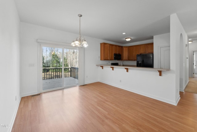 kitchen featuring a breakfast bar, black fridge, hanging light fixtures, kitchen peninsula, and light hardwood / wood-style floors